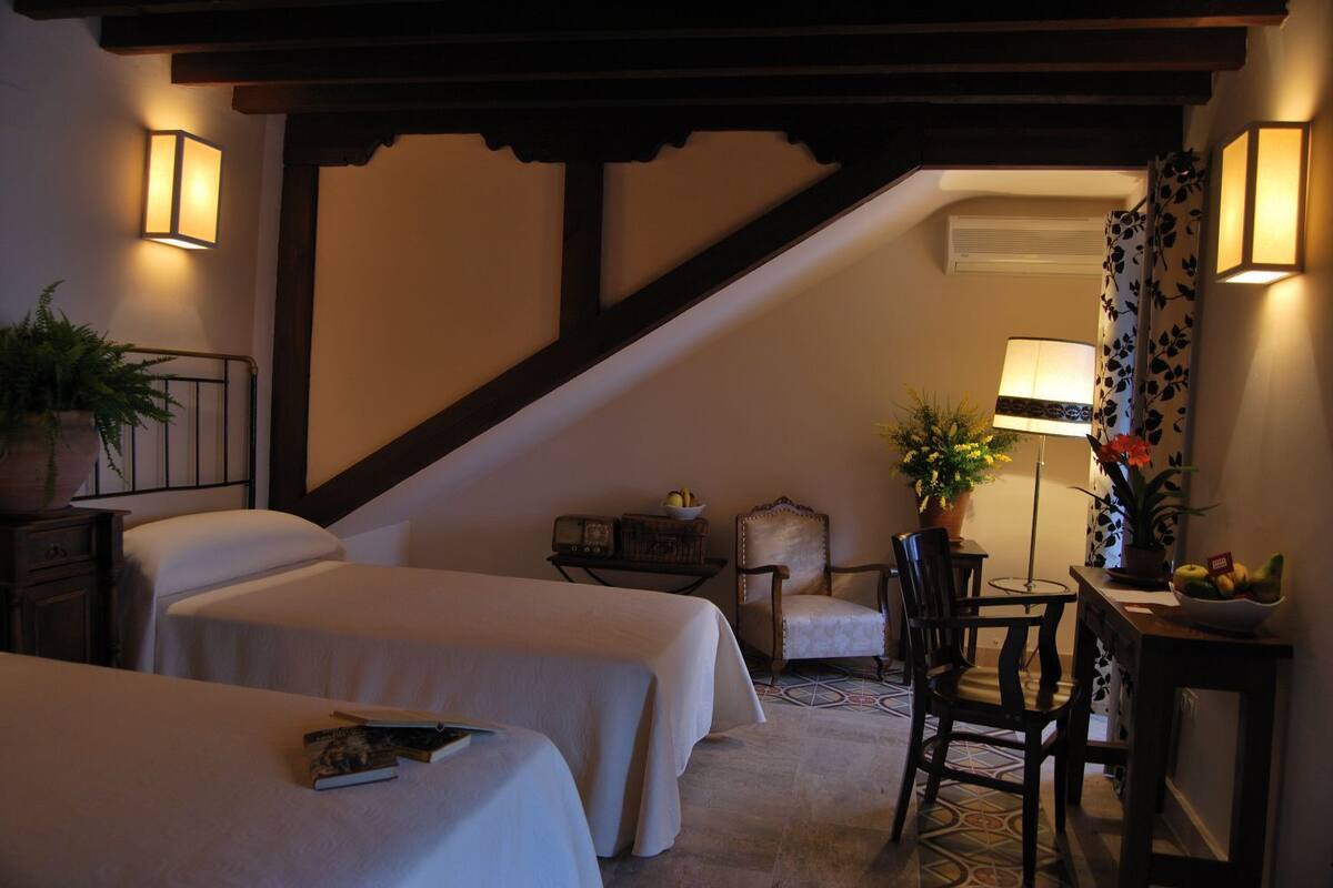 A hotel room with two beds, a desk, a chair, a lamp, and a potted plant.