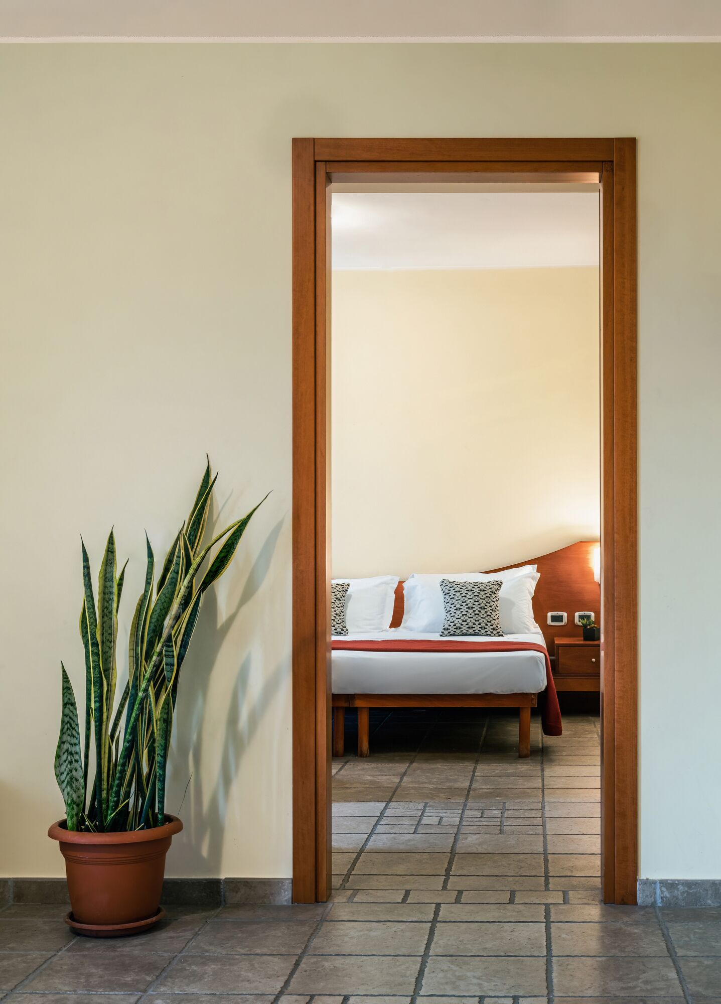 A doorway leading to a bedroom with a bed, a nightstand, and a potted plant.