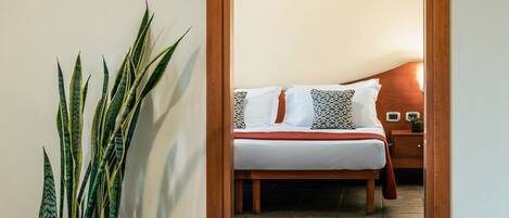 A doorway leading to a bedroom with a bed, a nightstand, and a potted plant.