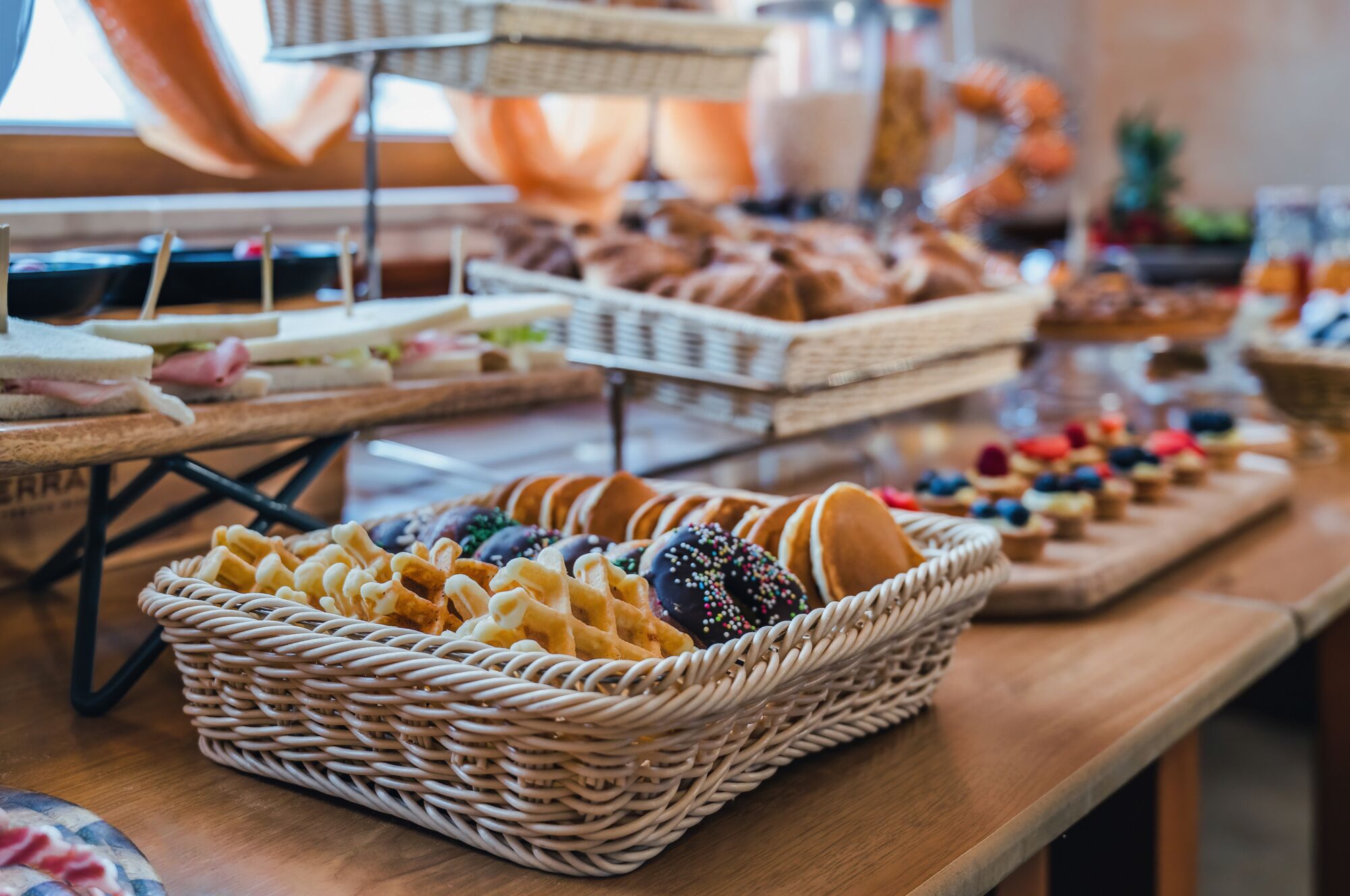Une table de buffet proposant divers plats, notamment des sandwichs, des pâtisseries et des beignets.