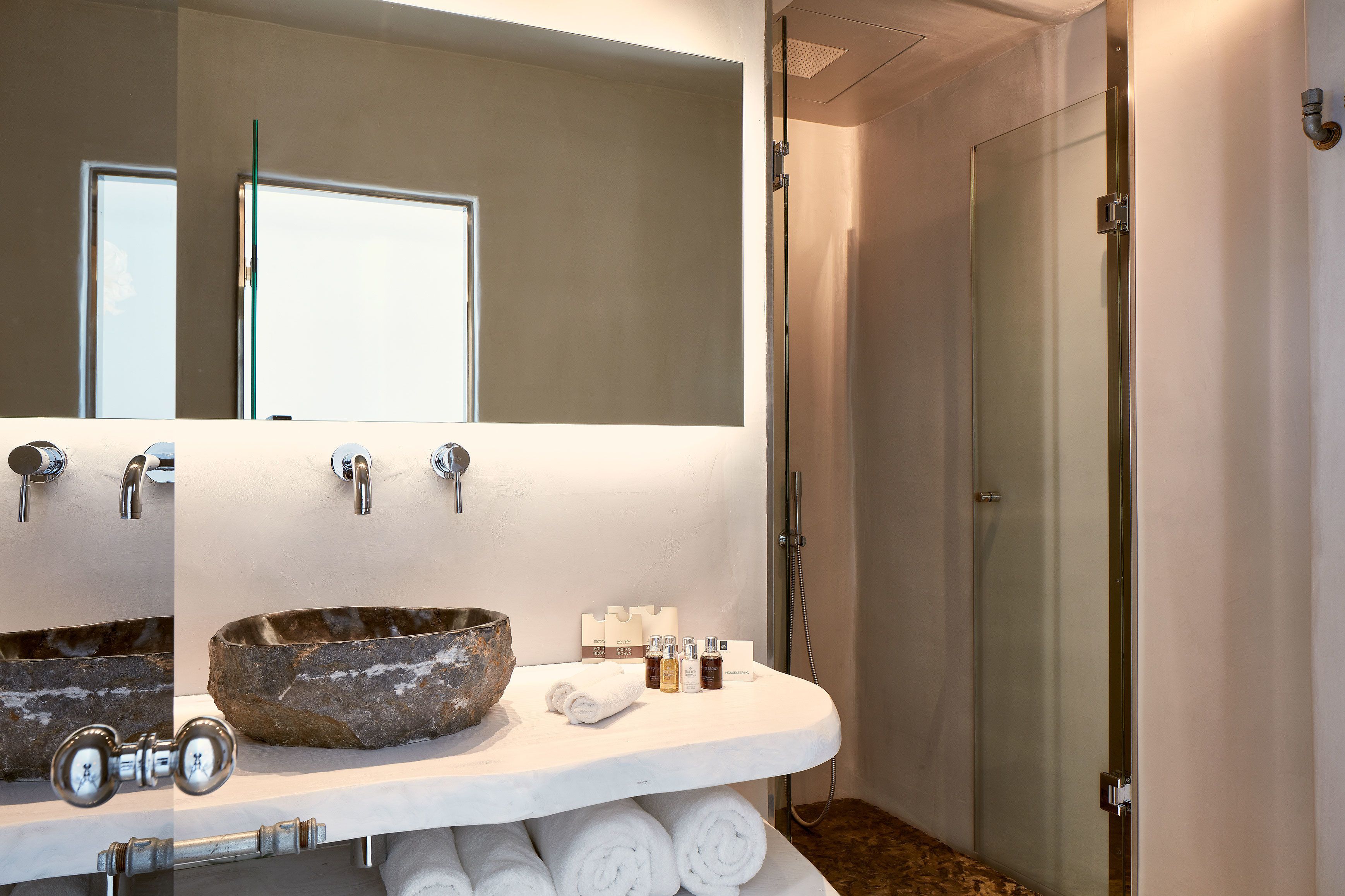 A bathroom with a large mirror, a stone basin, two sinks, and a glass-enclosed shower.