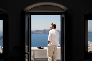 Un homme se tient à la porte d’un balcon, d’où l’on aperçoit la mer et des collines lointaines.