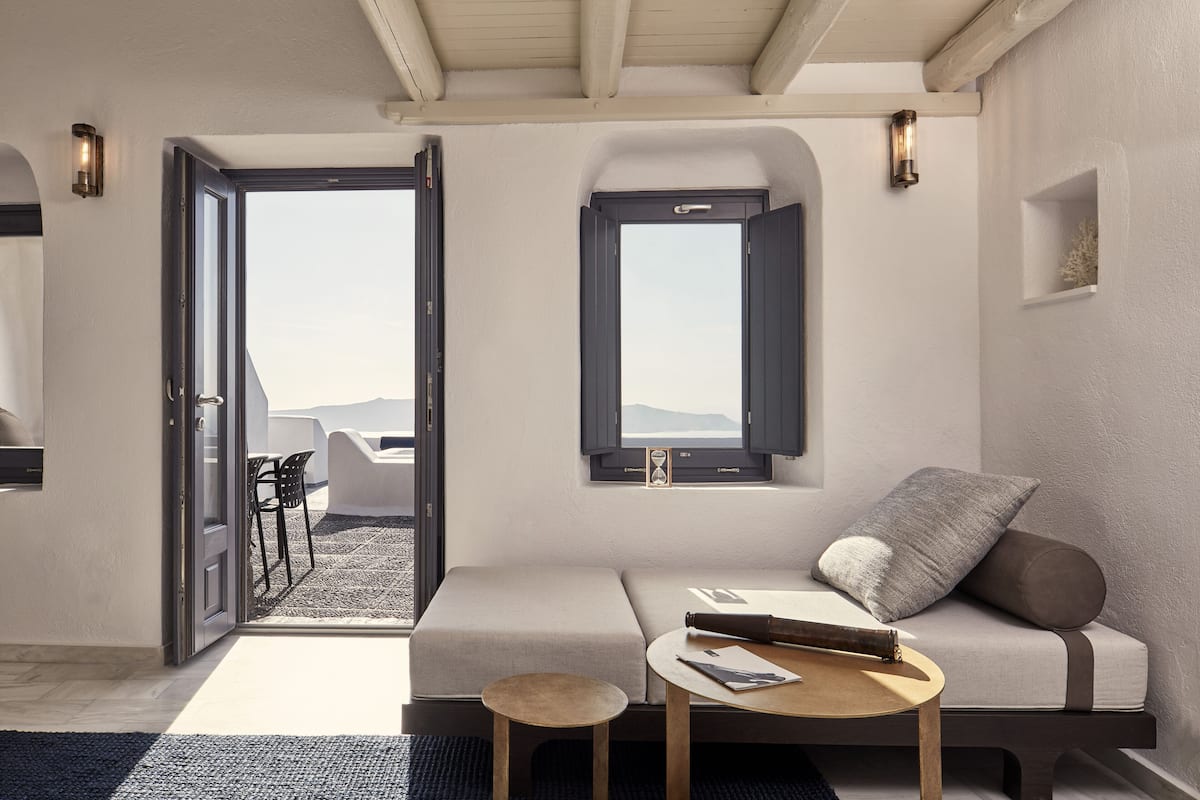 A modern living room with a sofa, a small round table, and a window with a view of the mountains.