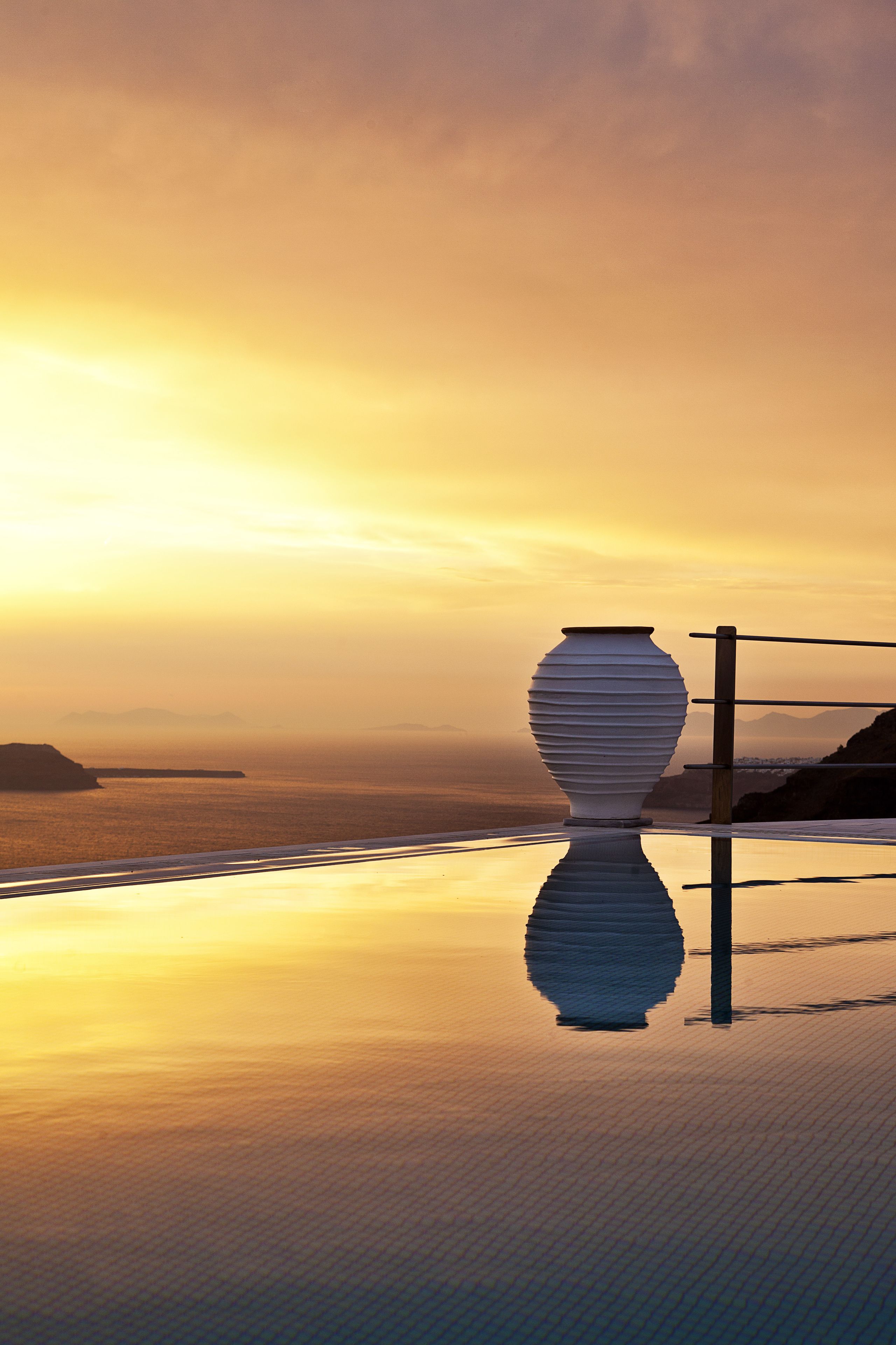 A large white vase on a reflective surface with a sunset view.