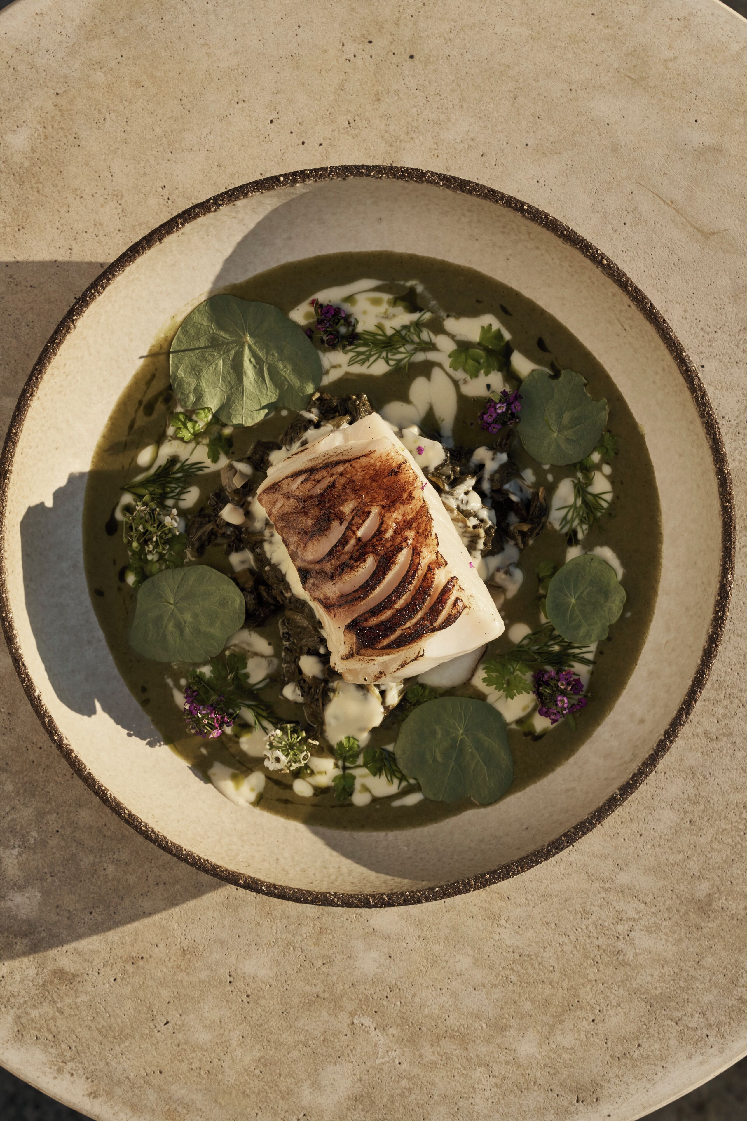 Un plato con pescado a la parrilla, verduras y flores comestibles.