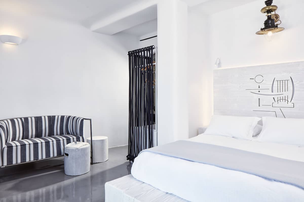 A modern hotel room with a bed, a striped sofa, a small round table, and a wall-mounted light fixture.
