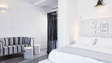 A modern hotel room with a bed, a striped sofa, a small round table, and a wall-mounted light fixture.