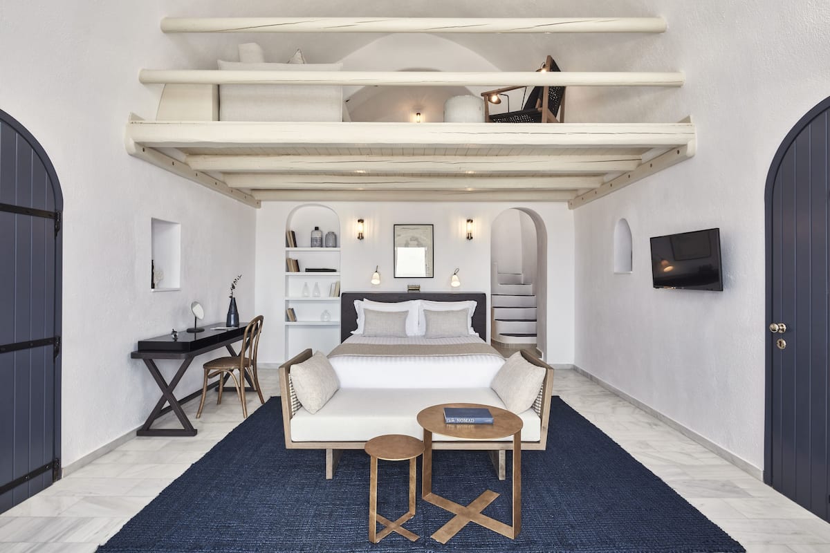 A bedroom with a bed, a desk, a chair, a small table, and a TV.