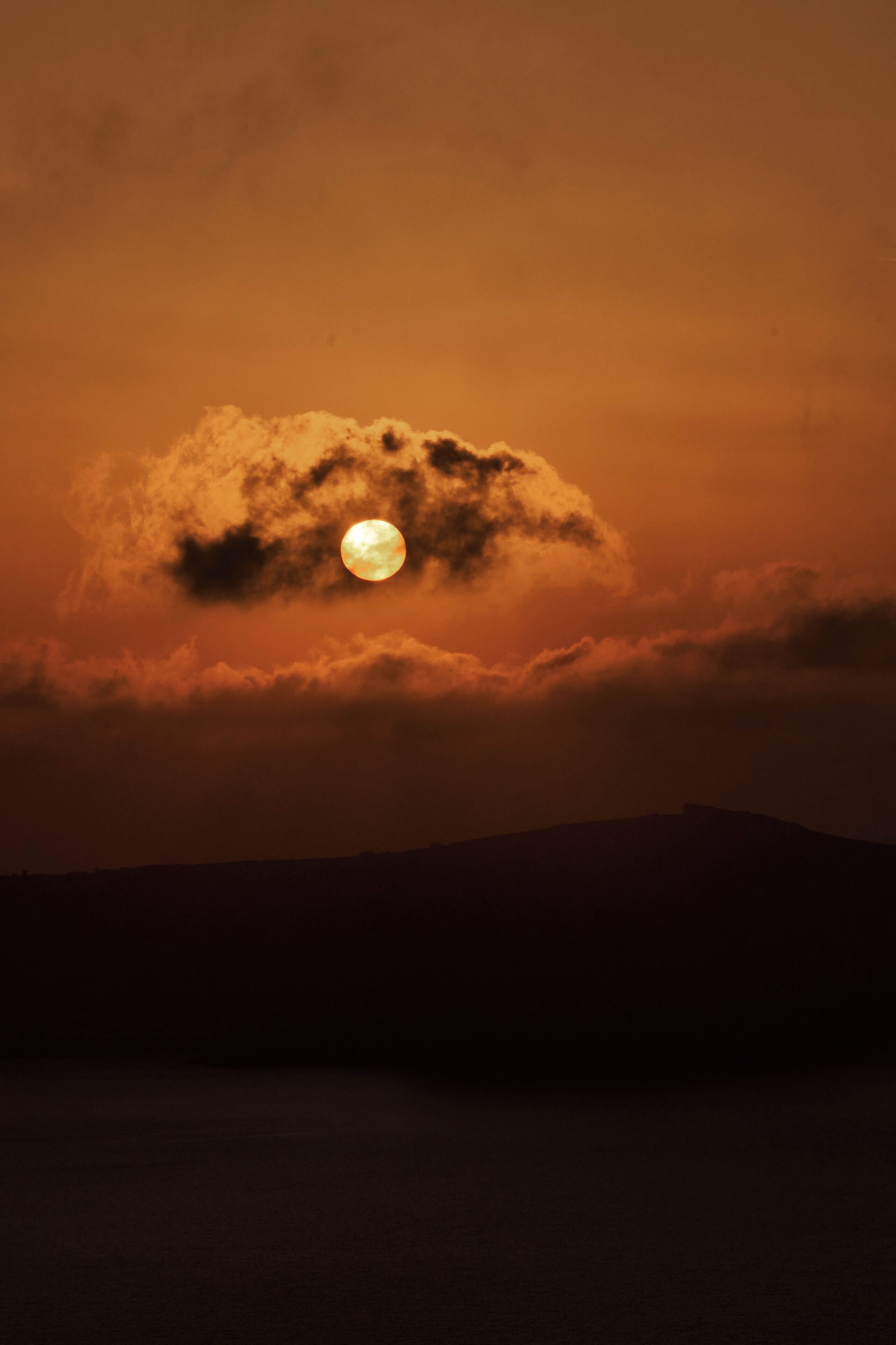 Luna parcialmente oculta por nubes, con la silueta de una cadena montañosa al frente.