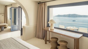 A balcony with a view of the sea, a table with a lamp, and a bed with patterned bedding. - Homeric Poems (Santorini)