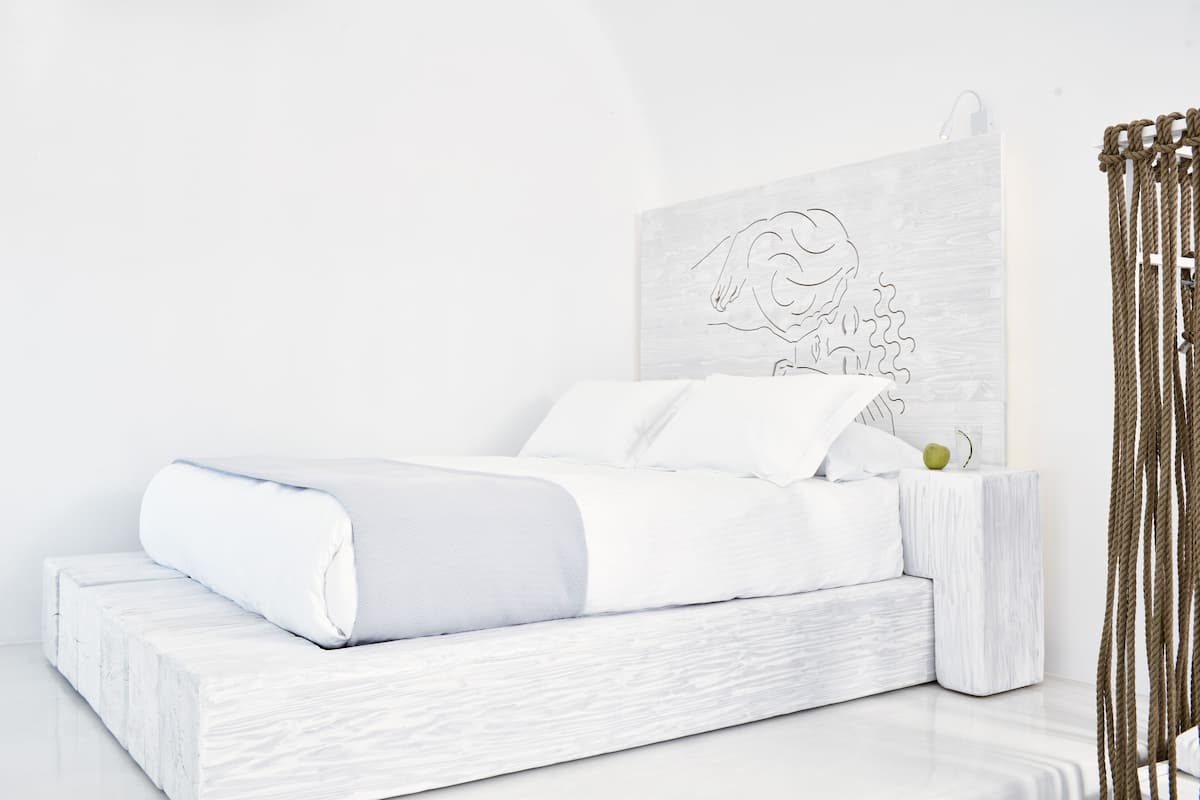 A minimalist bedroom with a white bed, a wooden headboard, and a simple artwork.