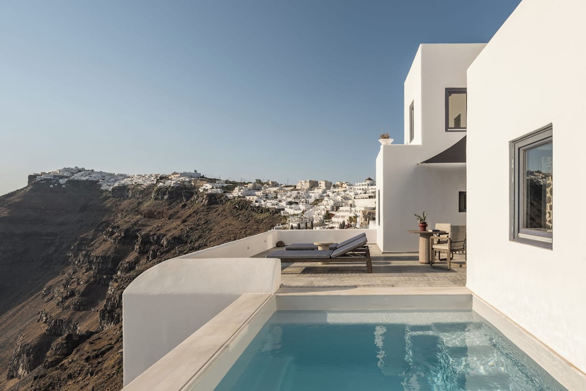 A modern building with a pool and a view of a white village on a hillside.