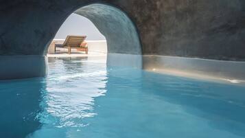 Uma piscina interna com uma espreguiçadeira sob uma grande estrutura em arco.