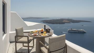 A balcony with a table set for breakfast overlooking the sea, featuring a cruise ship in the distance.