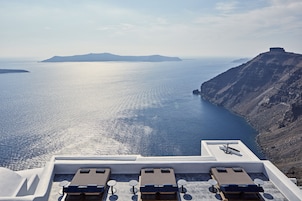 Terraza en la azotea con sillones de sol con vistas a un mar tranquilo y un paisaje montañoso.