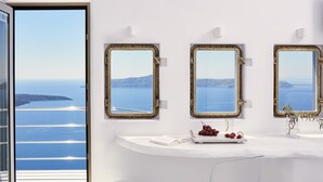 A bathroom with a white vanity, three ship porthole mirrors, and a view of the sea and islands. - Homeric Poems (Santorini)