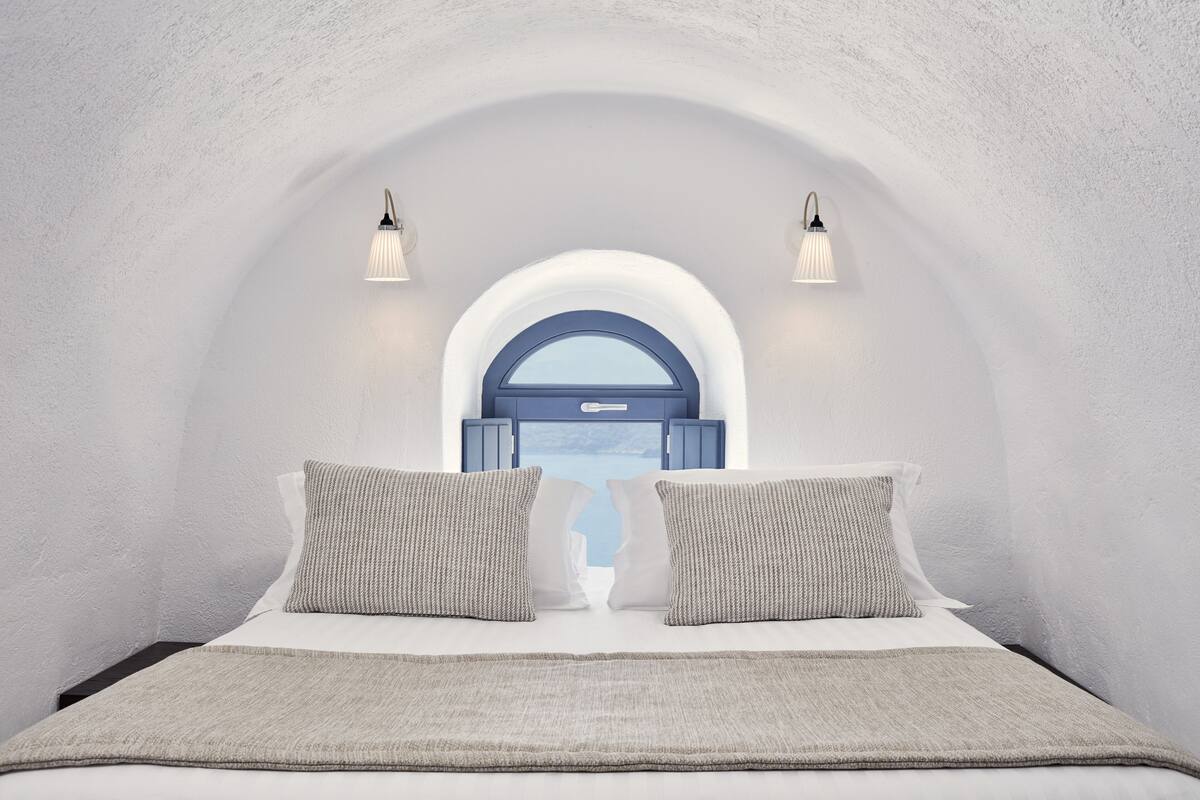A bedroom with a bed, two pillows, a blanket, and a window with a view.