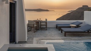 A pool area with lounge chairs and a table, overlooking a body of water and a distant island. - Homeric Poems (Santorini)