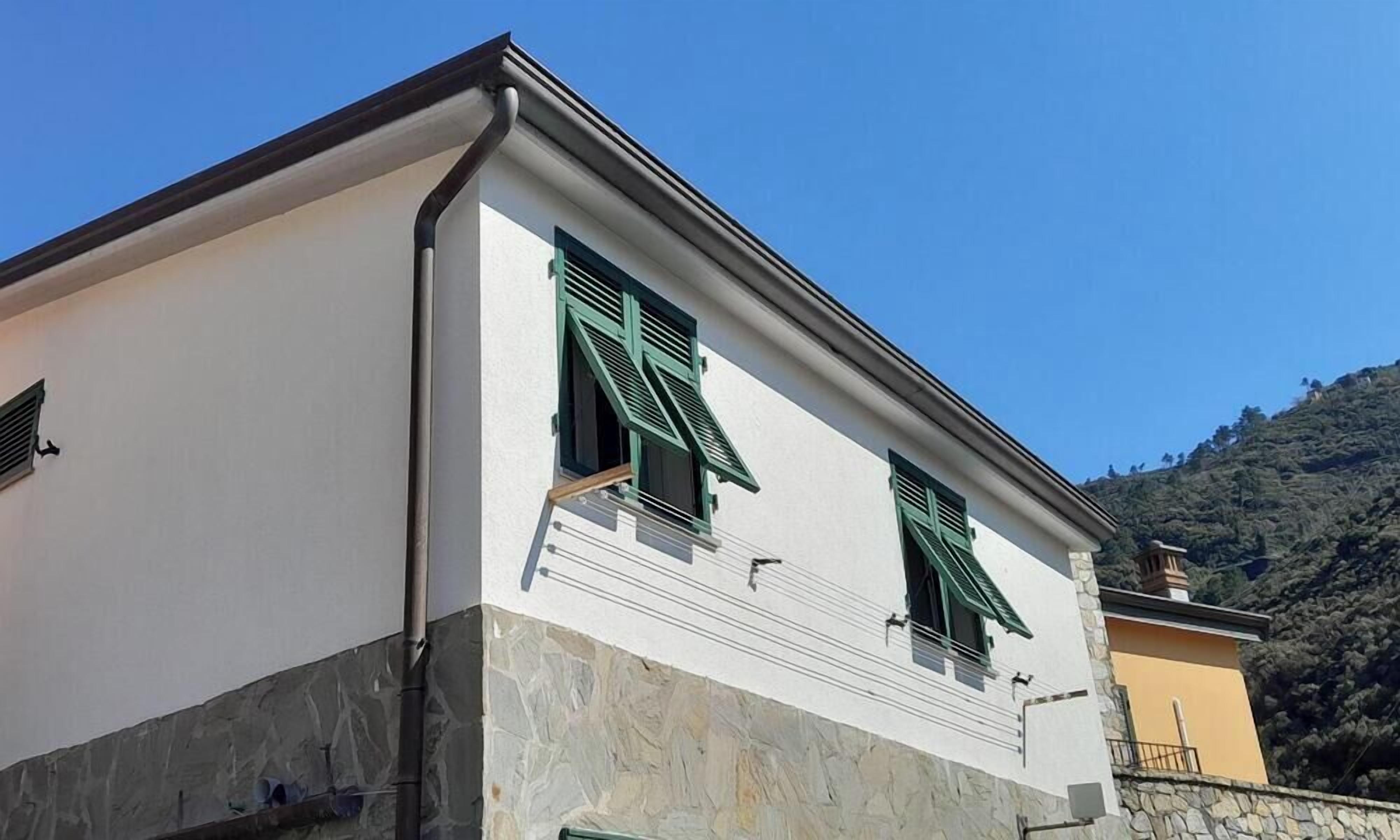 A building with a stone base, white upper walls, and green shutters.