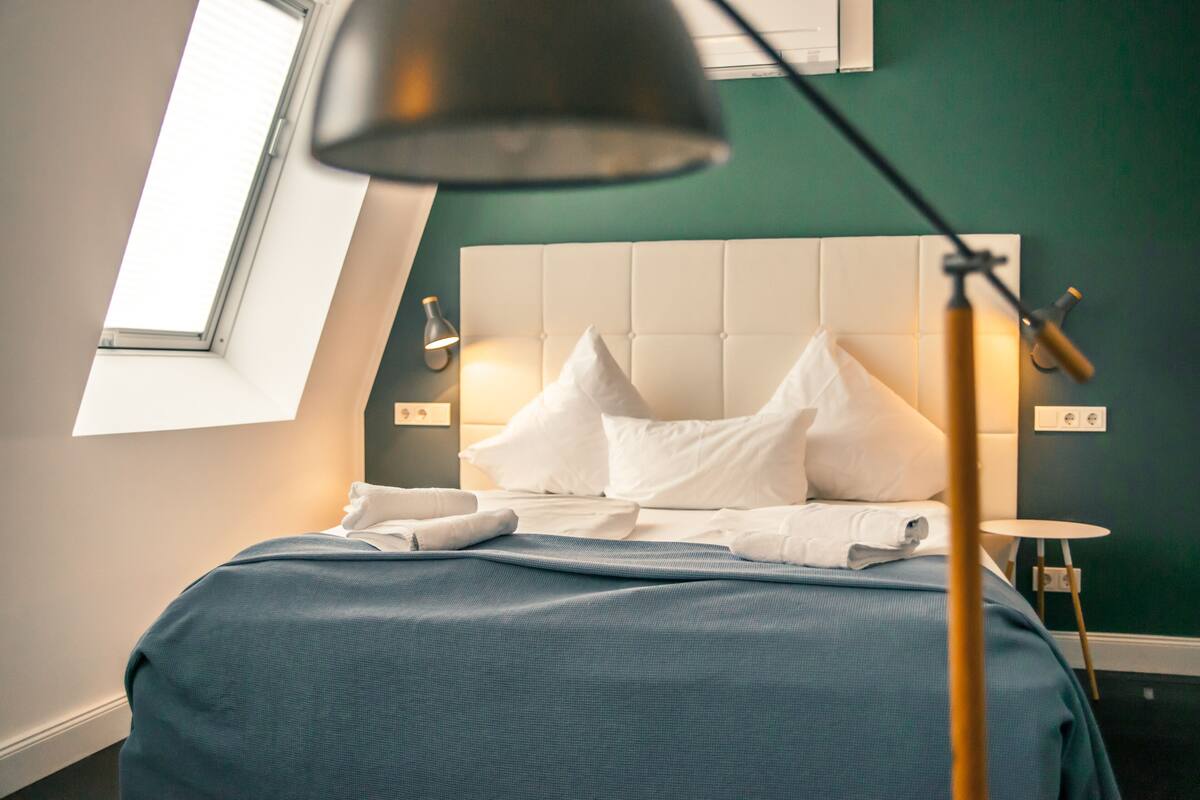 A neatly made bed with white linens and a blue blanket, a bedside lamp, and a small table with a lamp.