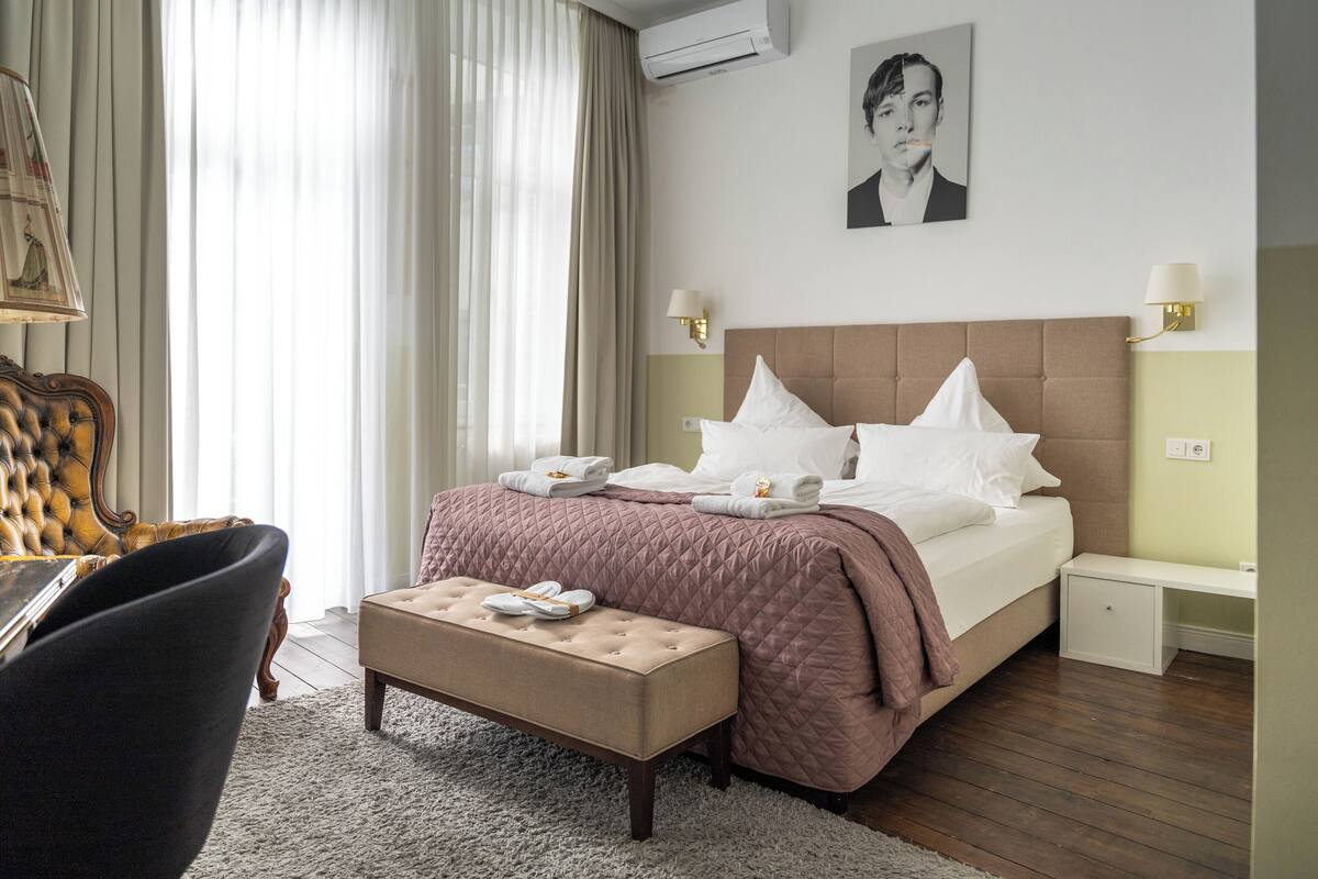 A hotel room with a large bed, a bedside table, a chair, and a desk.