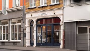 A building with a storefront labeled "marsil" featuring a dark blue entrance, white columns, and a brick facade.
