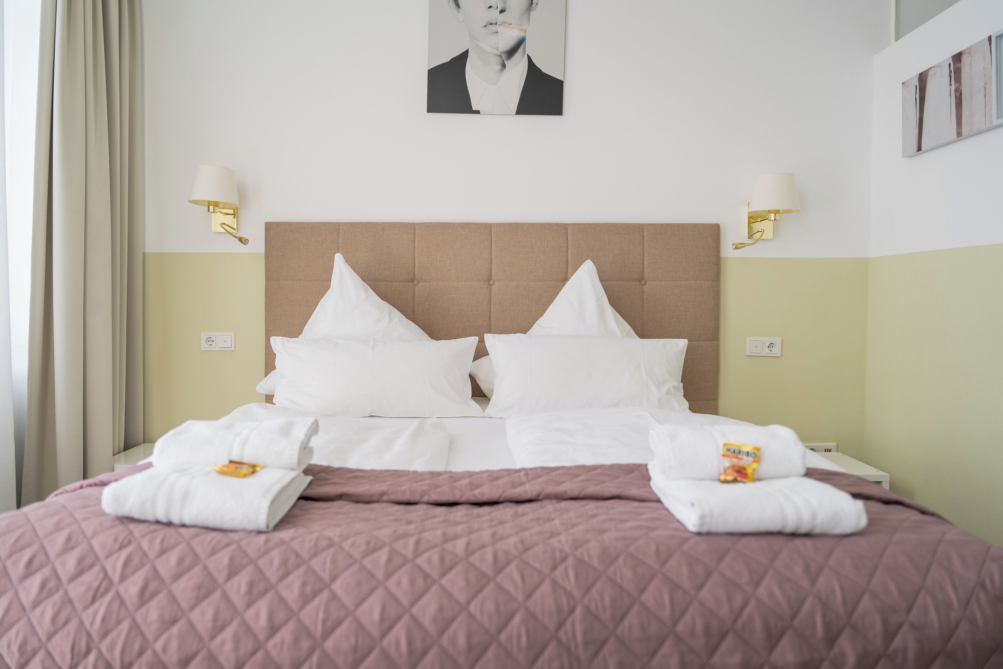 Een net opgemaakt bed met een gewatteerde roze dekbedovertrek, witte kussens en twee handdoeken aan het voeteneind.