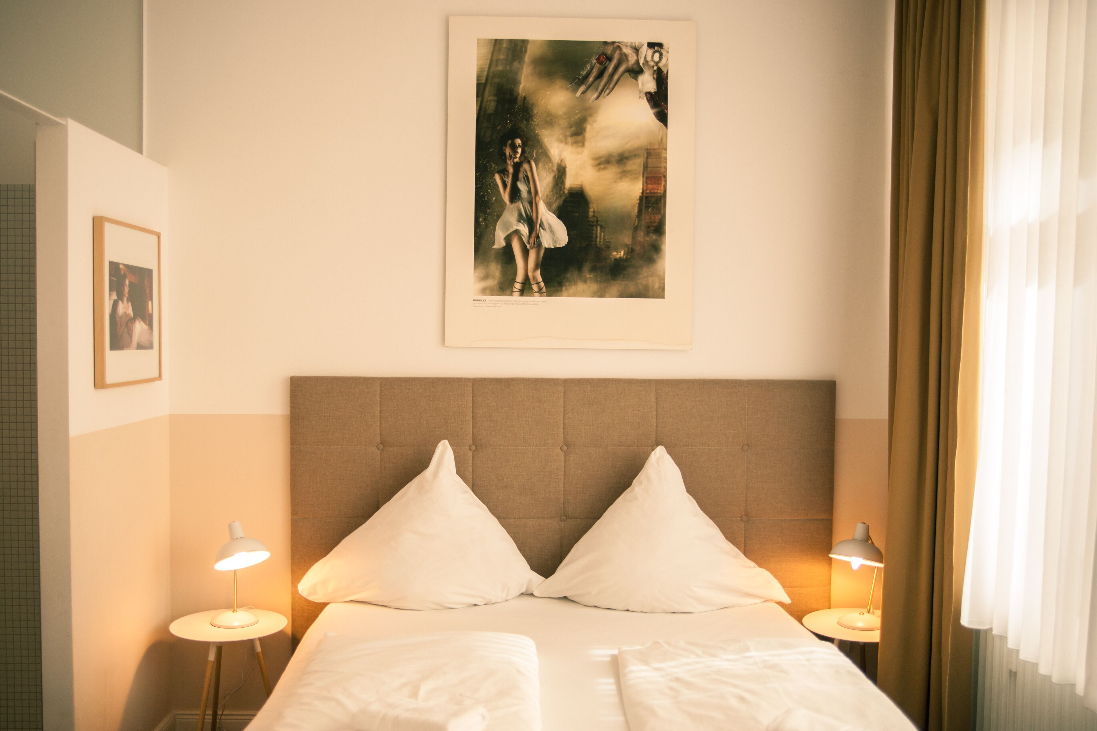 Camera d'albergo con un letto grande, due comodini con lampade, una testiera e un quadro appeso al muro.