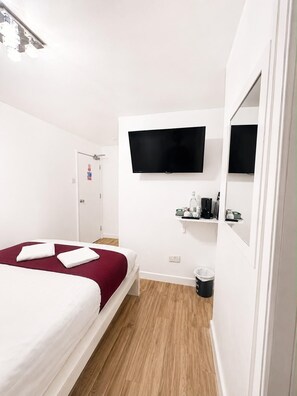 A hotel room with a bed, a television mounted on the wall, a small shelf with toiletries, and a door leading to another room. - King's Cross Hotel (London)