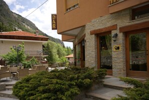 A bar with outdoor seating, stone facade, and a mountain backdrop. - Hotel Londra (Acceglio)