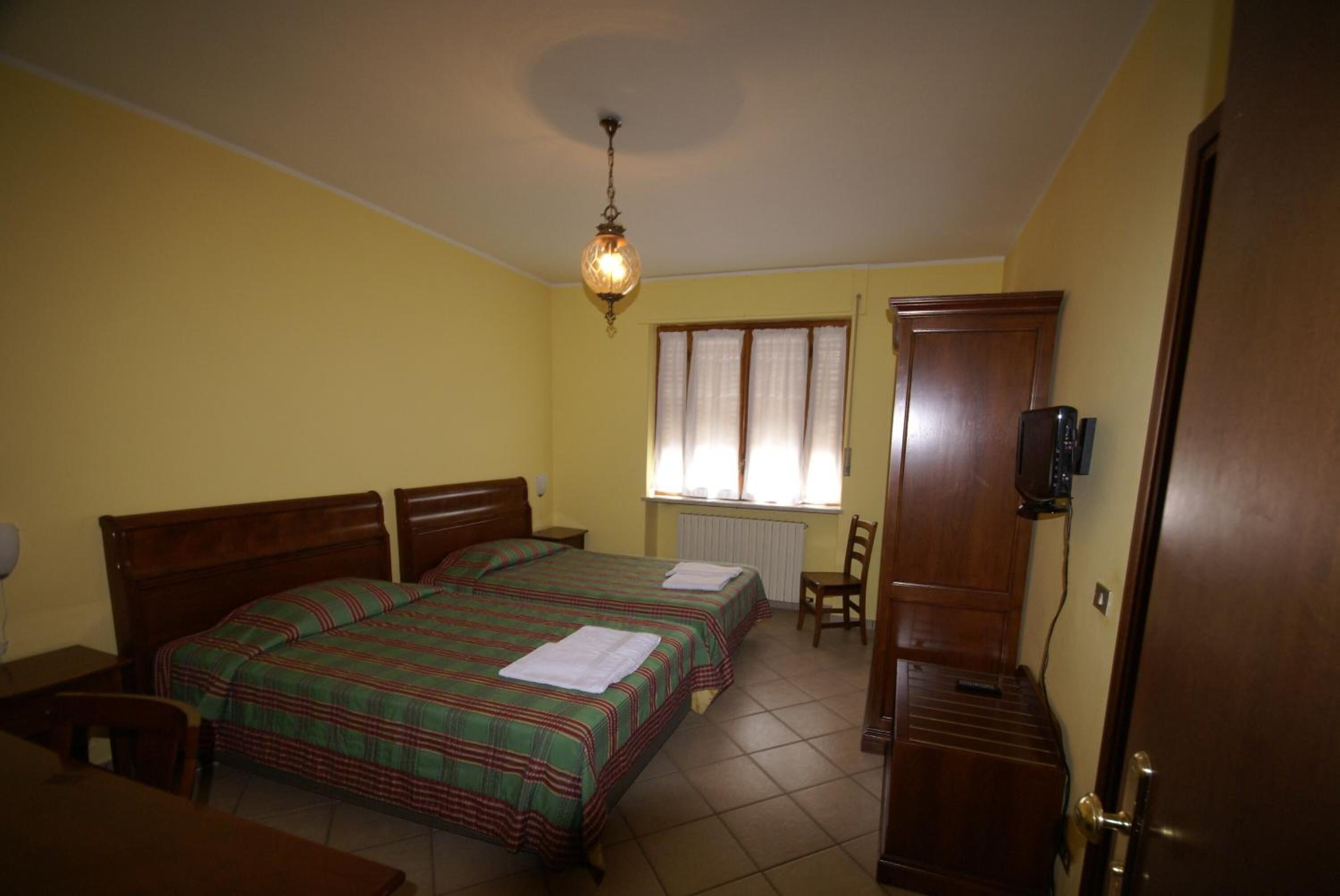 A bedroom with two single beds, a wooden wardrobe, a desk, and a chair.