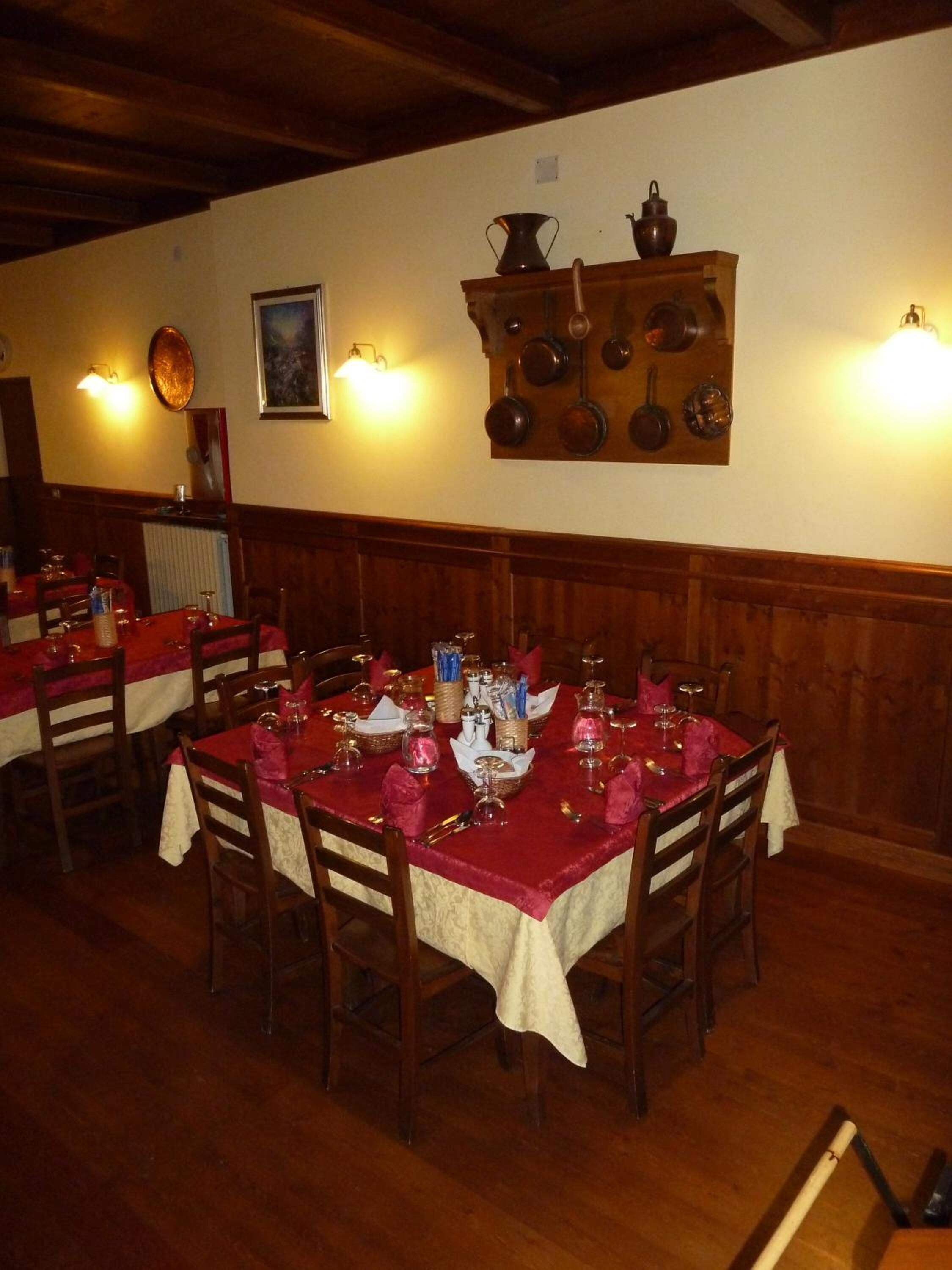 Ein Restaurant mit Holztischen, gedeckten Plätzen, einer an der Wand befestigten Kochgeschirr-Halterung und Wandleuchten, die Licht spenden.
