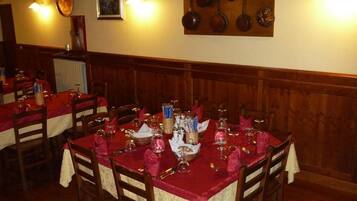 Ein Restaurant mit Holztischen, gedeckten Plätzen, einer an der Wand befestigten Kochgeschirr-Halterung und Wandleuchten, die Licht spenden.
