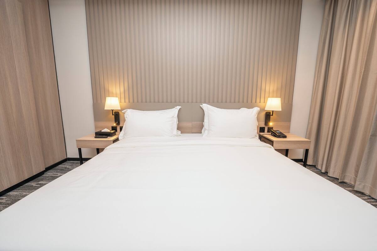 Une chambre d’hôtel avec un grand lit, deux tables de chevet avec des lampes et une tête de lit ornée de lignes verticales.