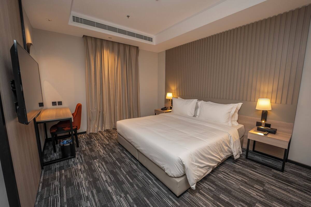 Une chambre d’hôtel avec un grand lit, un bureau avec une chaise, une télévision et une table de chevet avec une lampe.