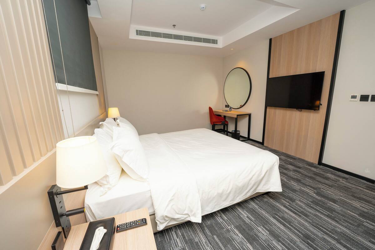 Une chambre d’hôtel comprenant un lit, une table de chevet, une lampe, une télévision et un petit bureau avec une chaise.