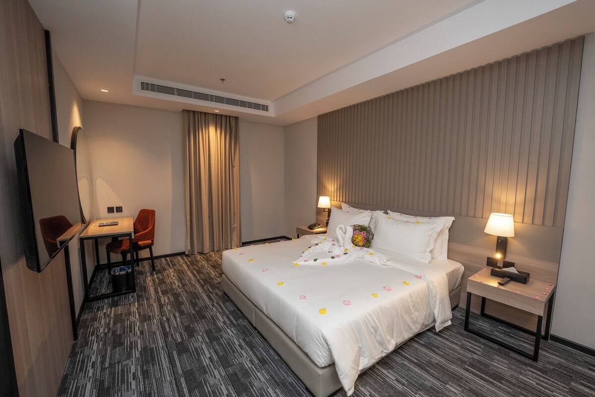 Une chambre d’hôtel avec un grand lit, un bureau avec une chaise, une télévision et une table de chevet avec une lampe.
