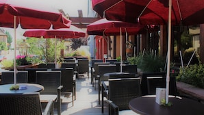 Un espace extérieur aménagé avec des chaises en osier et des parasols rouges.