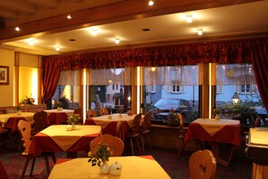 Un restaurant doté de nombreuses tables et chaises, de grandes fenêtres avec des rideaux et offrant une vue sur la rue.