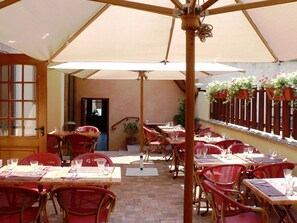 Une terrasse extérieure avec des tables et des chaises, des parasols et des plantes en pot.
