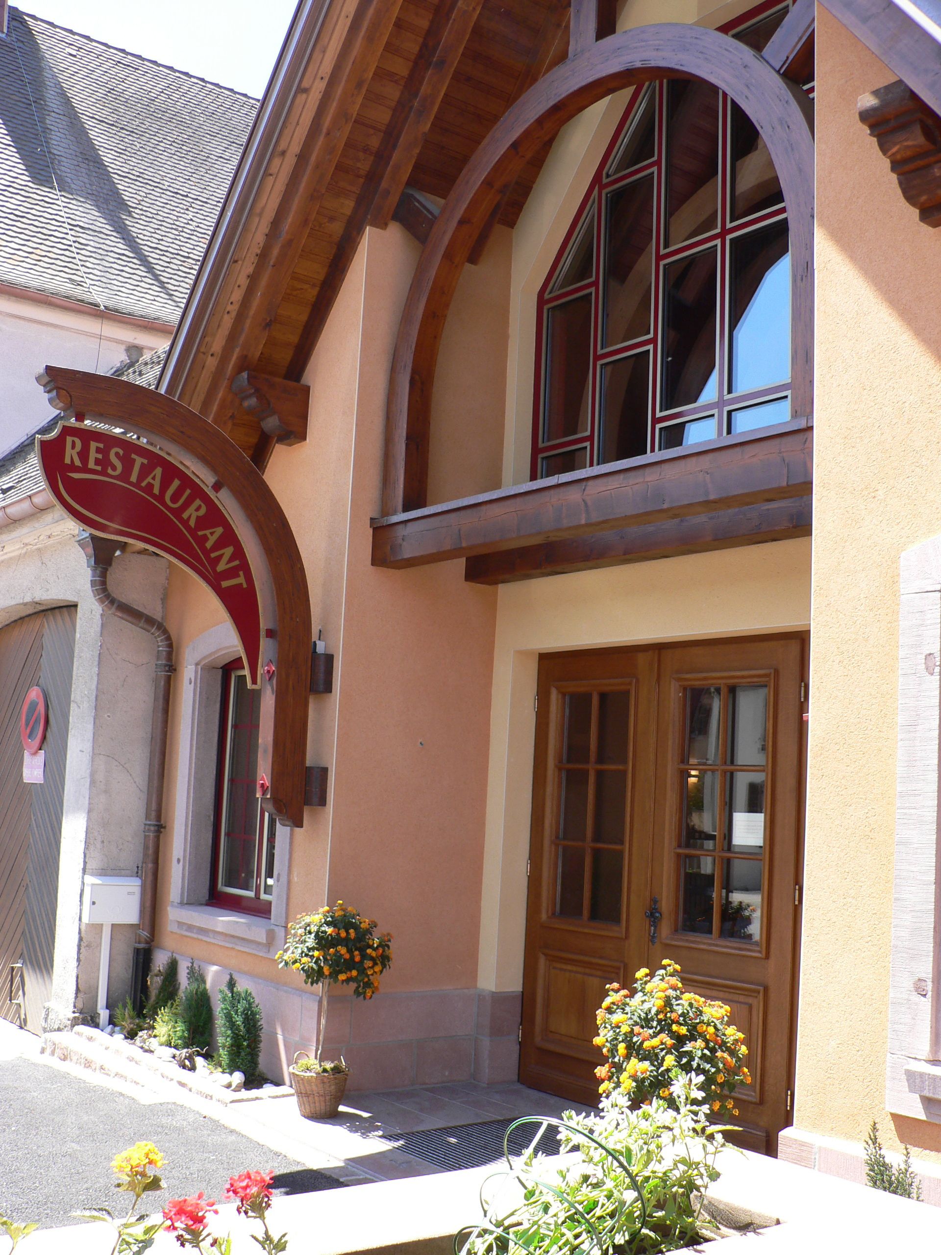 A restaurant with a wooden facade, a red sign, and a large arched window.