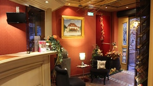Un hall d’entrée avec un comptoir de réception, un tableau encadré, une chaise, une petite table avec une lampe et un escalier.
