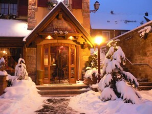 A snow-covered building with a wooden entrance, steps leading up to the door, and snow-covered trees.