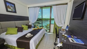 A hotel room with a bed, a desk with a computer, a TV, and a view of the ocean. - Hotel Solymar (Puerto Ayora)