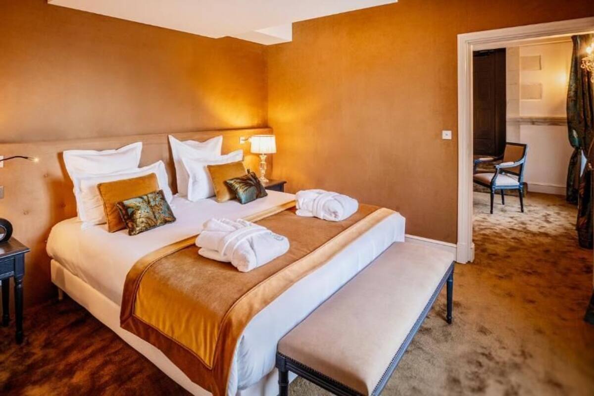 A hotel room with a large bed, a bedside table with a lamp, and a bench.