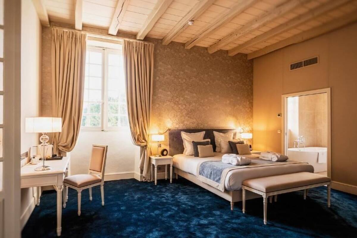 A bedroom with a bed, bedside tables, a desk, and a chair. There is a window with curtains, a door, and a mirror.