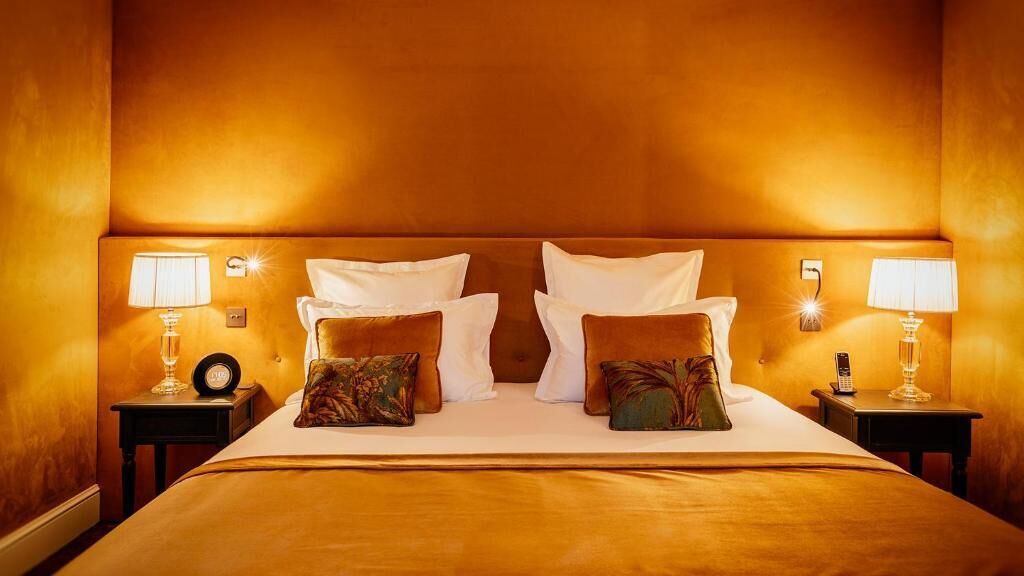 A hotel room with a large bed, two bedside tables with lamps, and a wall-mounted light fixture.