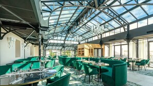 Un restaurante con techo de vidrio, asientos tapizados en verde y una estructura central de madera.
