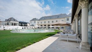 Un patio con piscina, mobiliario exterior y un edificio grande de arquitectura clásica.