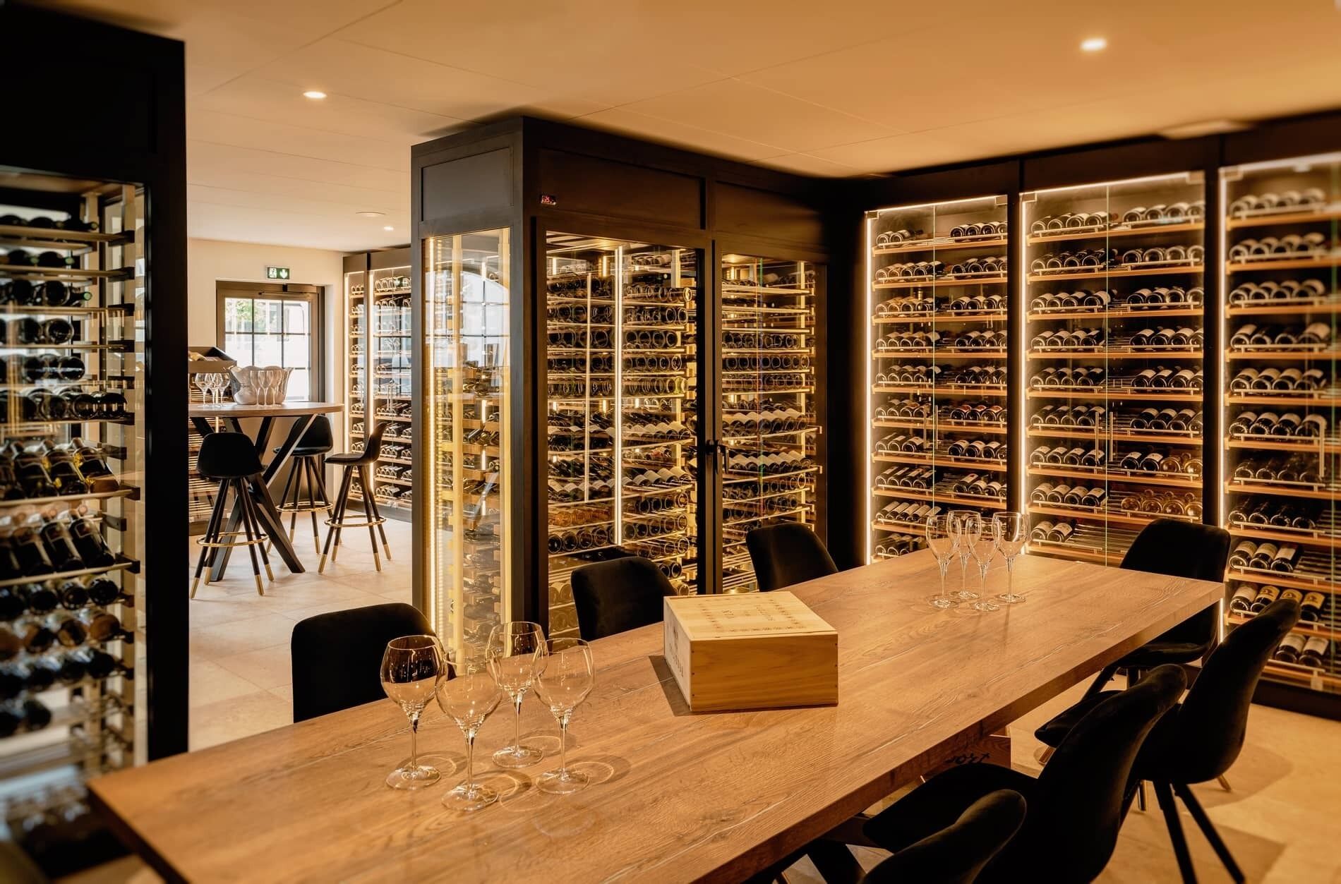 A wine cellar with rows of wine bottles and a long table with wine glasses.